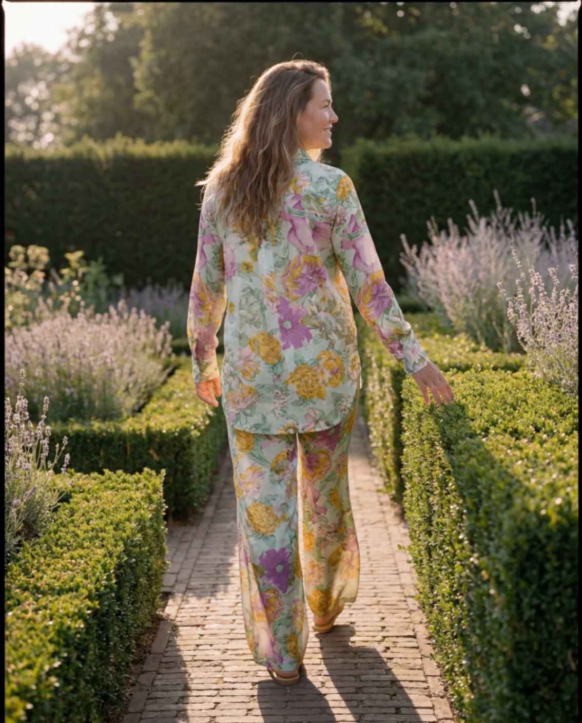 Model in bloemige outfit loopt door formele tuin